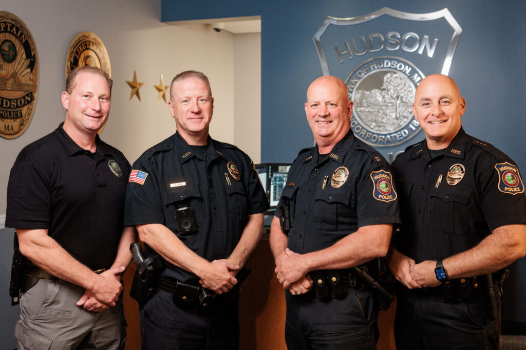 Four white male police officers in front of the Hudson Police Seal.