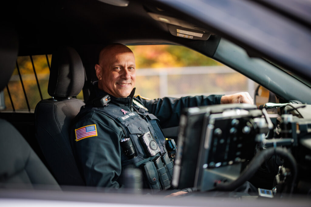A white male police officer sits in a police cruiser.