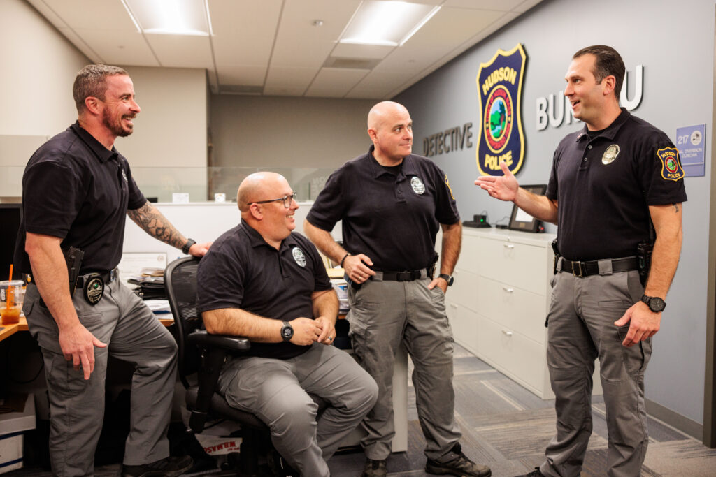 Four white men stand around talking in the Hudson Police headquarters.