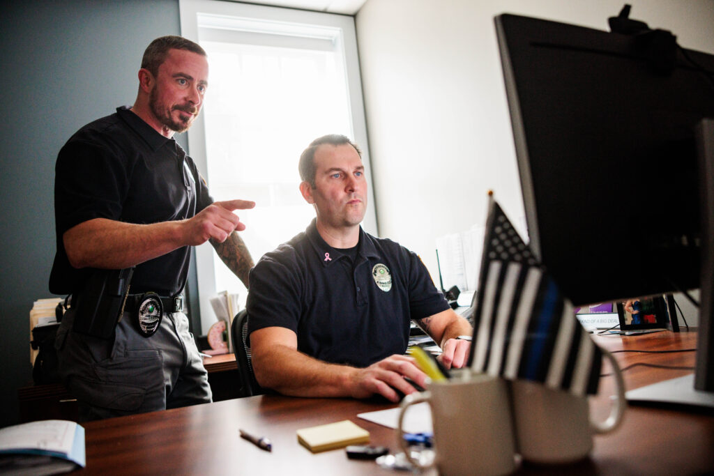 Two white men look at a computer screen.