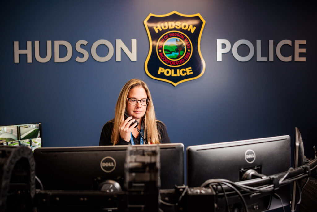 A white woman holds a phone while looking at two computer screens.