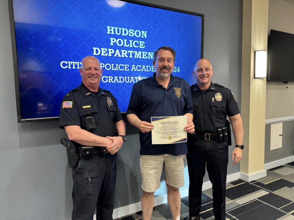 Citizens Police Academy participant holds a certificate while posing for a photo with two Hudson Police officers.