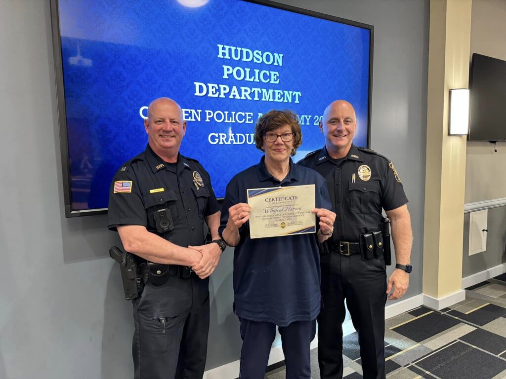 Citizens Police Academy participant holds a certificate while posing for a photo with two Hudson Police officers.