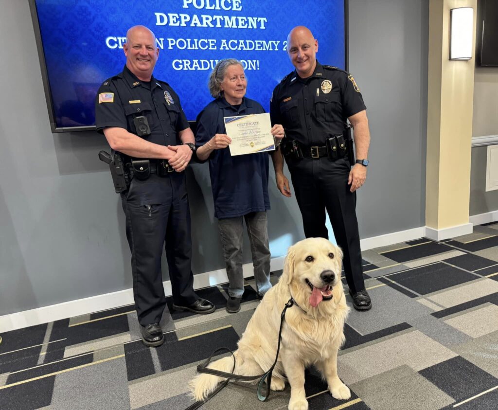 Citizens Police Academy participant holds a certificate while posing for a photo with two Hudson Police officers.