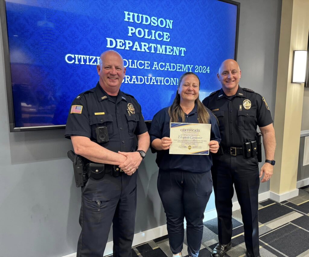 Citizens Police Academy participant holds a certificate while posing for a photo with two Hudson Police officers.