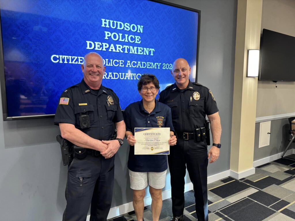 Citizens Police Academy participant holds a certificate while posing for a photo with two Hudson Police officers.