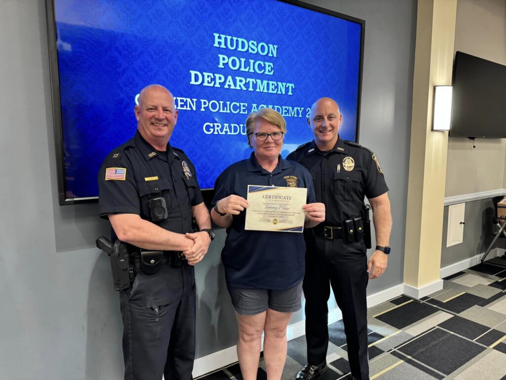 Citizens Police Academy participant holds a certificate while posing for a photo with two Hudson Police officers.